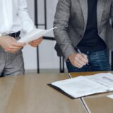 mężczyzna podpisuje dokumenty w towarzystwie prawnika